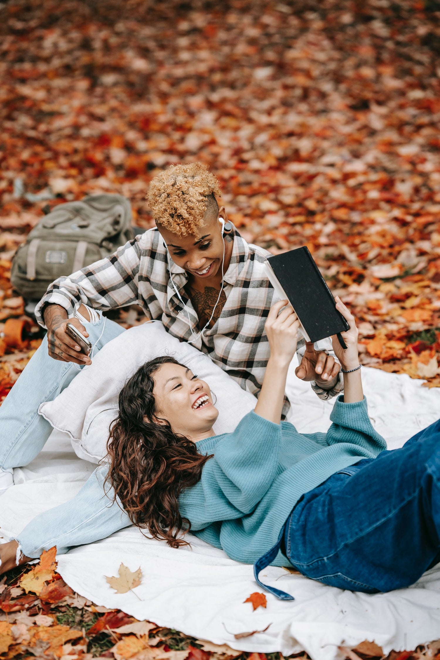 Two ladies laying on the ground with fall leaves reading - Quill Hawk Publishing in Edmond, OK